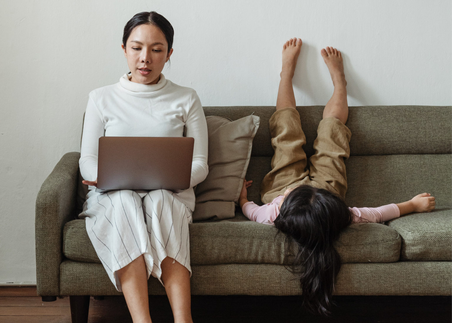 Woman sitting on sofa working with child next to her